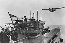 An RCN crew handles the surrendered U-889 off Shelburne, Nova Scotia, as a Royal Canadian Air Force (RCAF) Canso flying boat passes overhead.